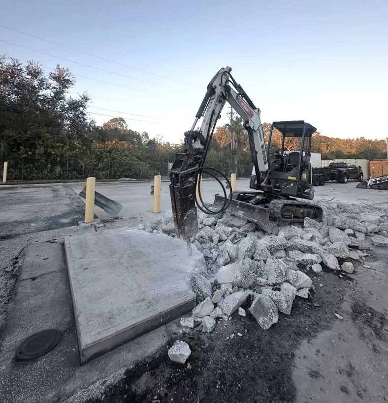 Excavator breaking out an old concrete slab for replacement