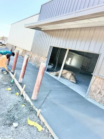 Crew finishing a fresh concrete apron along a metal building with bollards set