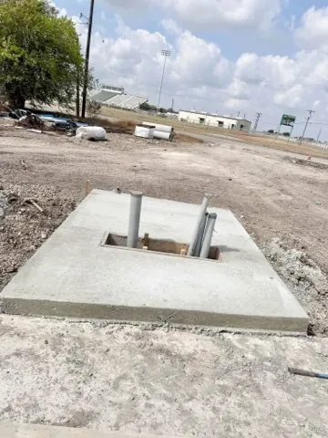 Finished equipment pad poured around steel post anchors near a stadium